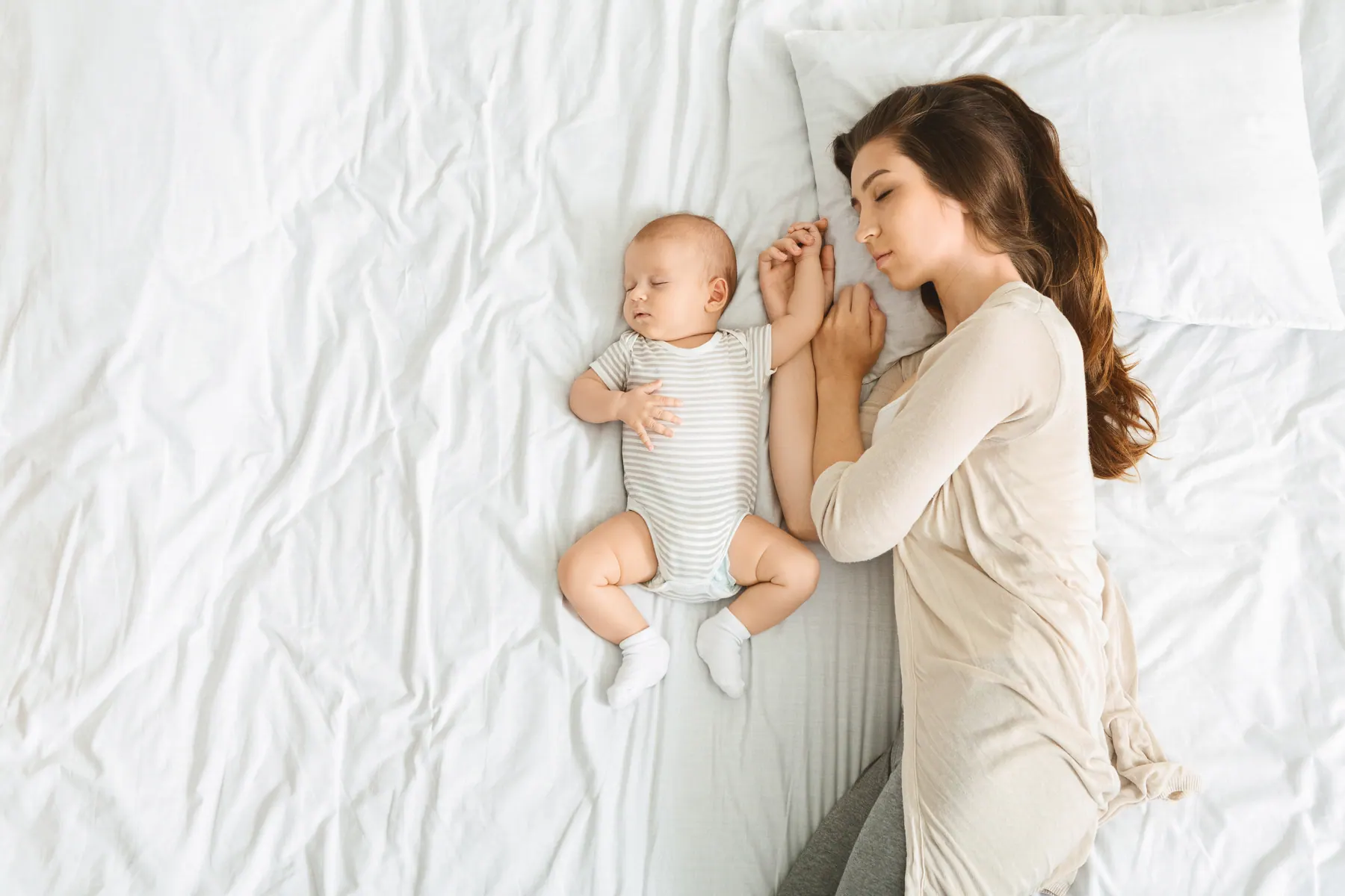 Mutter und Baby schlafen nebeneinander im hellen Bett