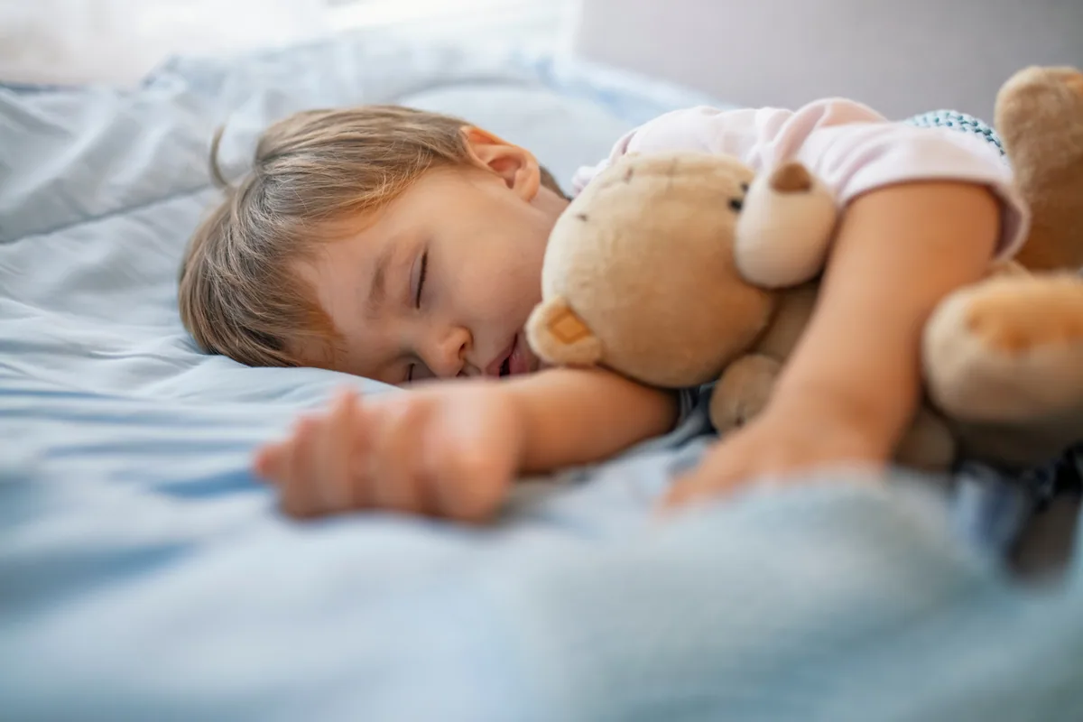 Kleinkind schläft mit dem Arm um einen Teddybären