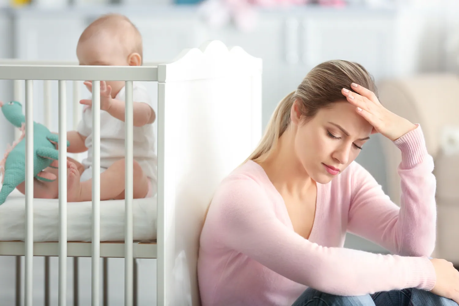 Erschöpfte Mutter sitzt neben dem Babybett